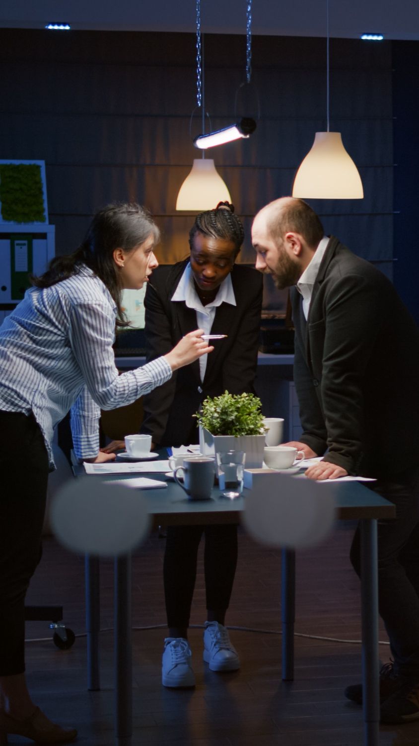 Three diverse professionals intensely discuss data during a late-night office meeting.