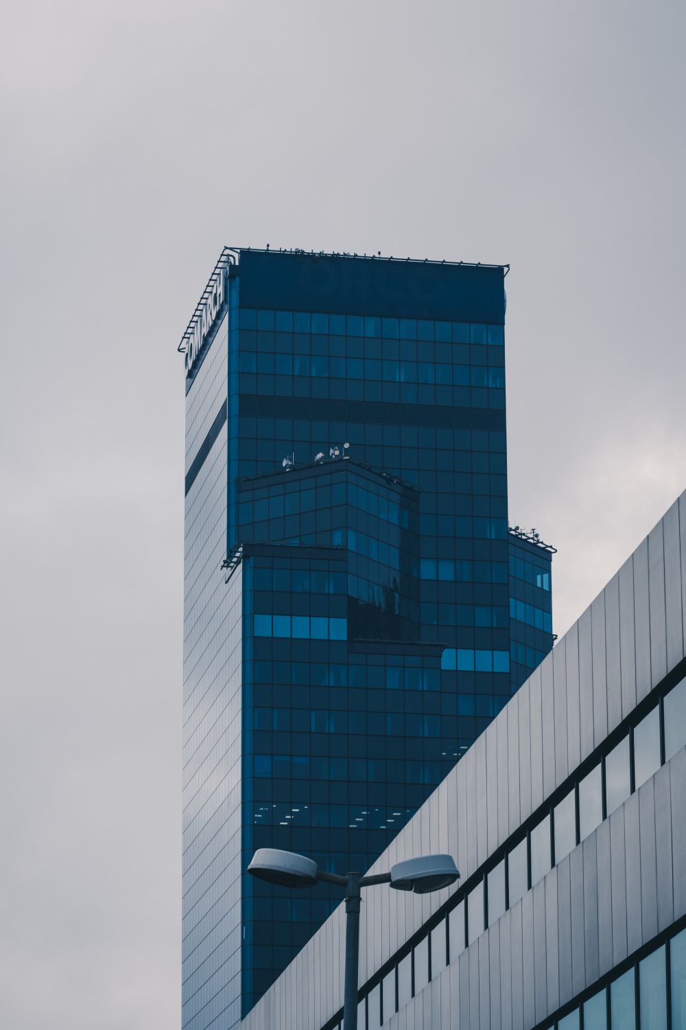 Tall, modern dark blue glass skyscraper against an overcast sky.